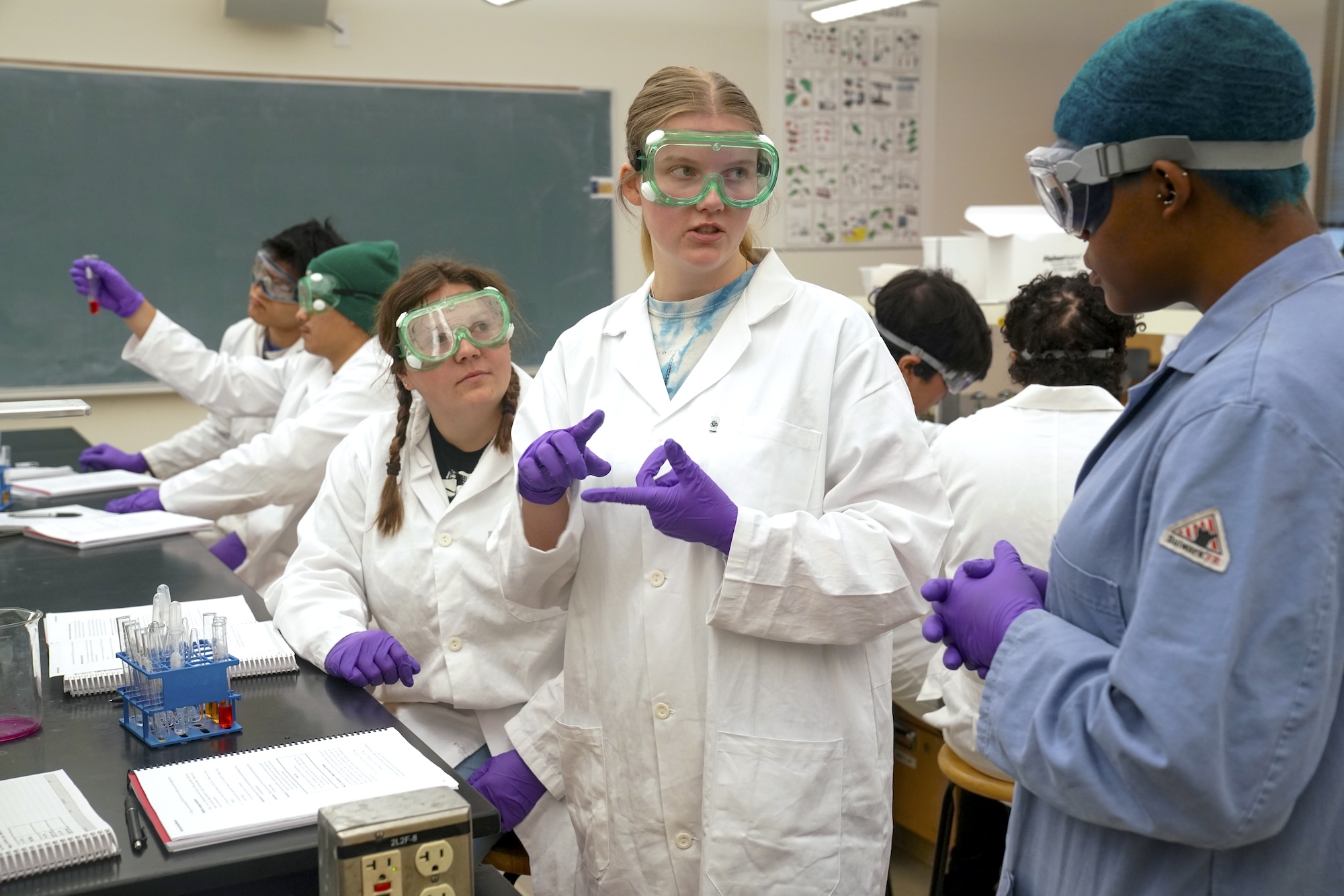 A group of students in coats and goggles in a lab