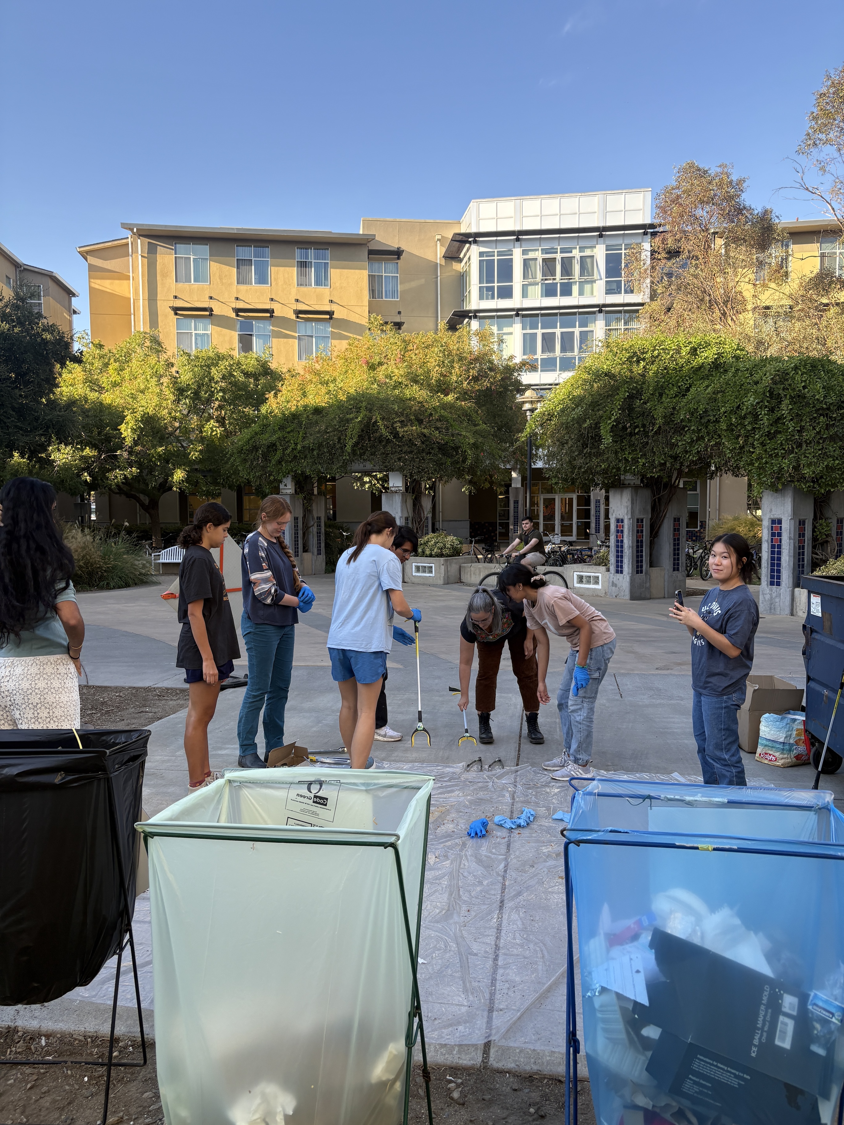 A group of people look at disposed gloves laid out on plastic on the floor outside