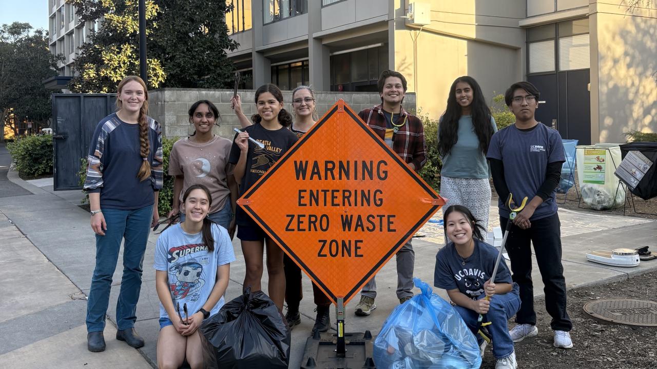 Students pose with trash bags and a sign that reads "Warning Entering Zero Waste Zone"