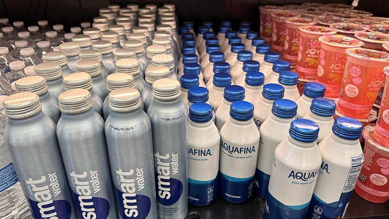 Image of drinks in an open, grab and go refrigerator. The drinks include smart water and Aquafina water bottled in aluminum screw-top cans.  