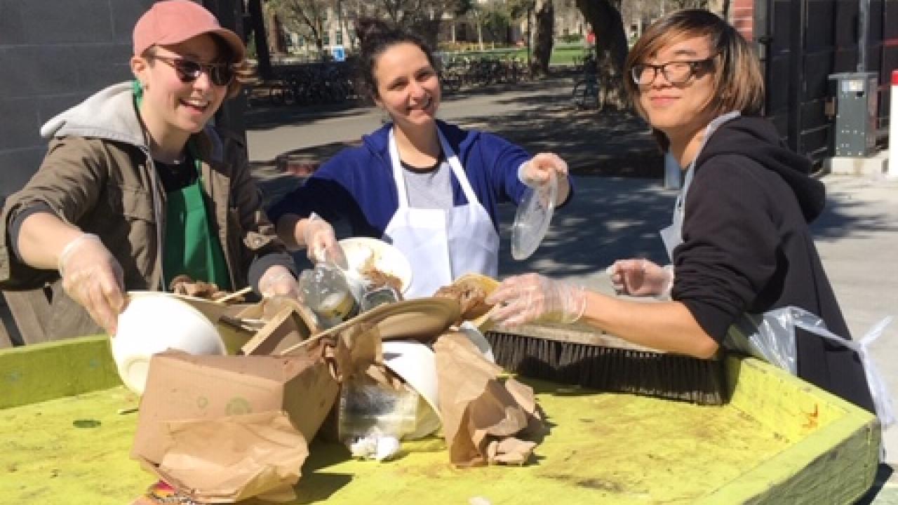 Three smiling students sorting waste at a CoHo waste audit.