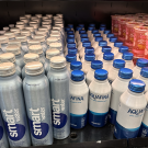 Image of drinks in an open, grab and go refrigerator. The drinks include smart water and Aquafina water bottled in aluminum screw-top cans.  