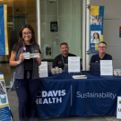 Five students at a campus sustainability table with signs and brochures