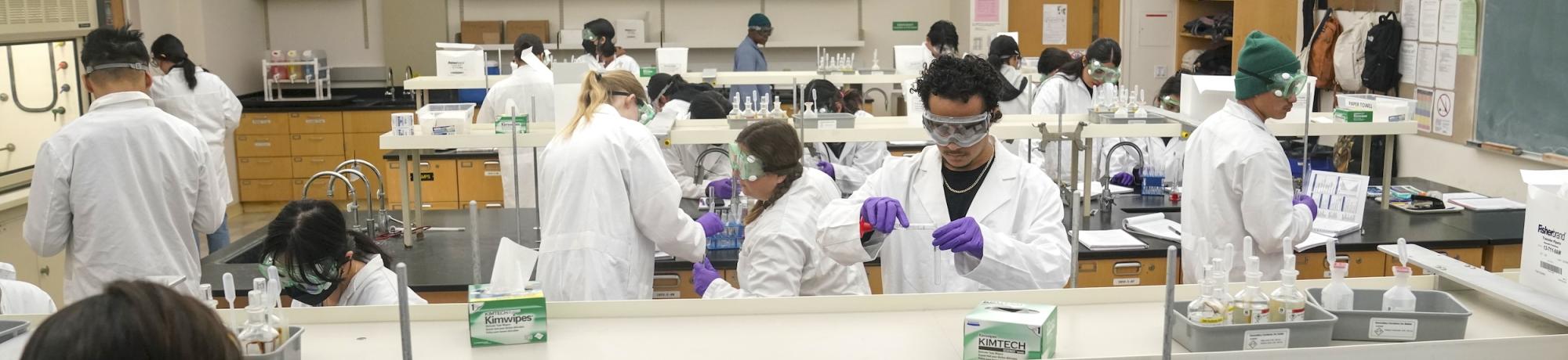 Group of students wearing lab coats in goggles in a lab